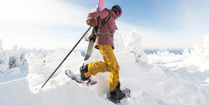Male with snowboard strapped to his back, using snowshoes and poles to search for some fresh powder. Mad Dog's Ski and Board carries a variety of snowshoes and snowshoe accessories for all your winter adventuring!
